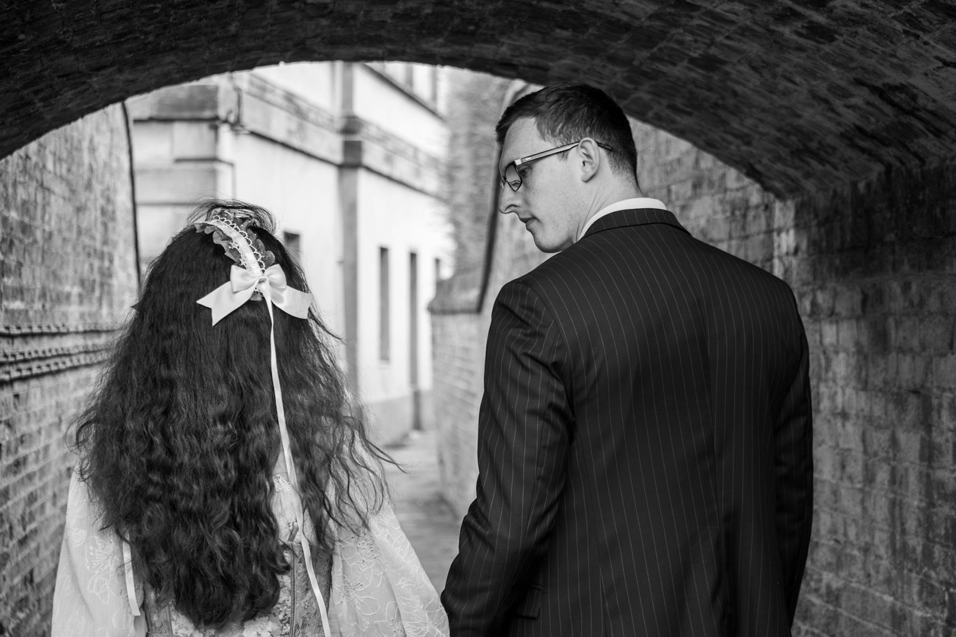 Bride and groom beneath a brick archway, in black and white