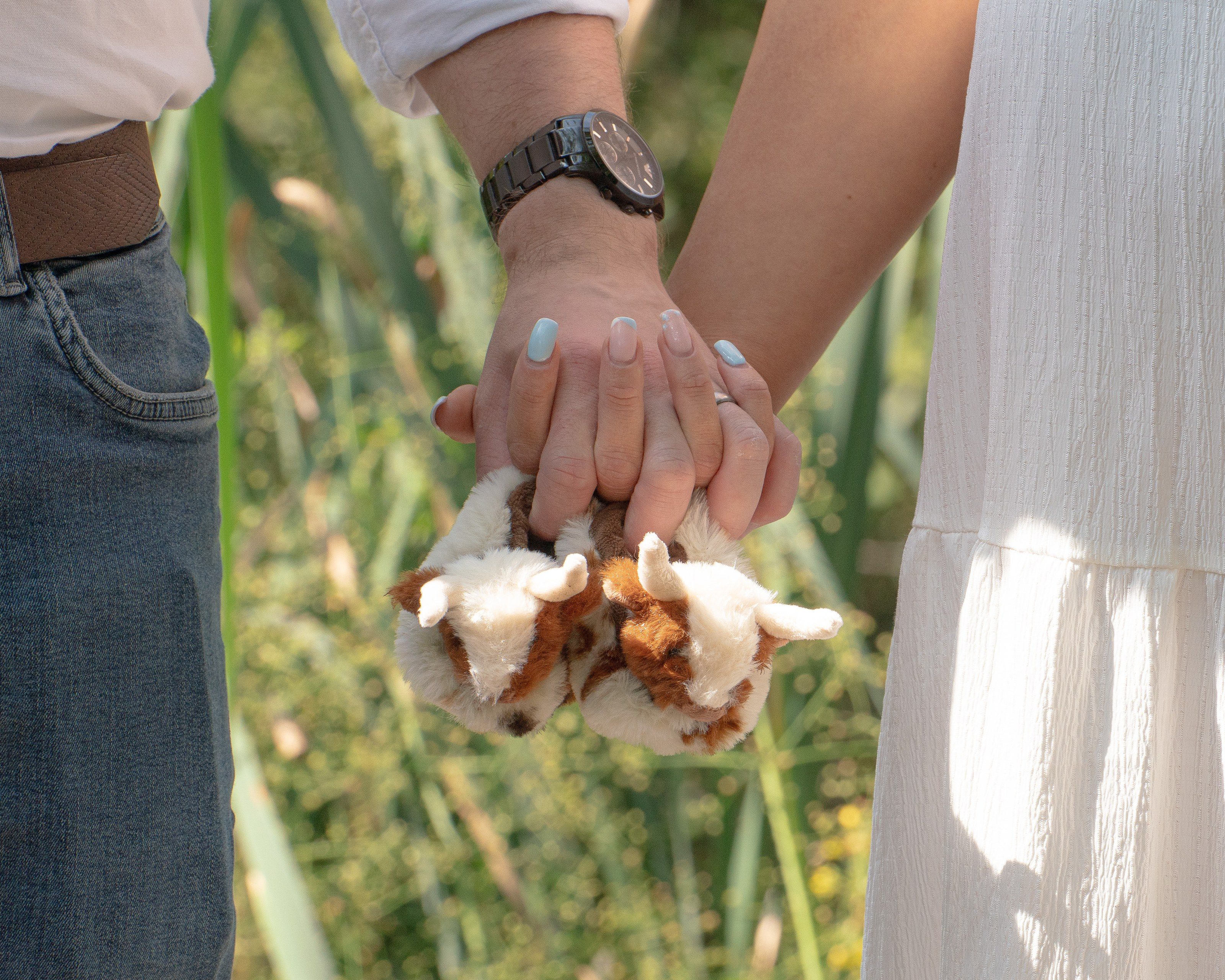 Couple’s hands hold a pair of tiny booties in the long grass