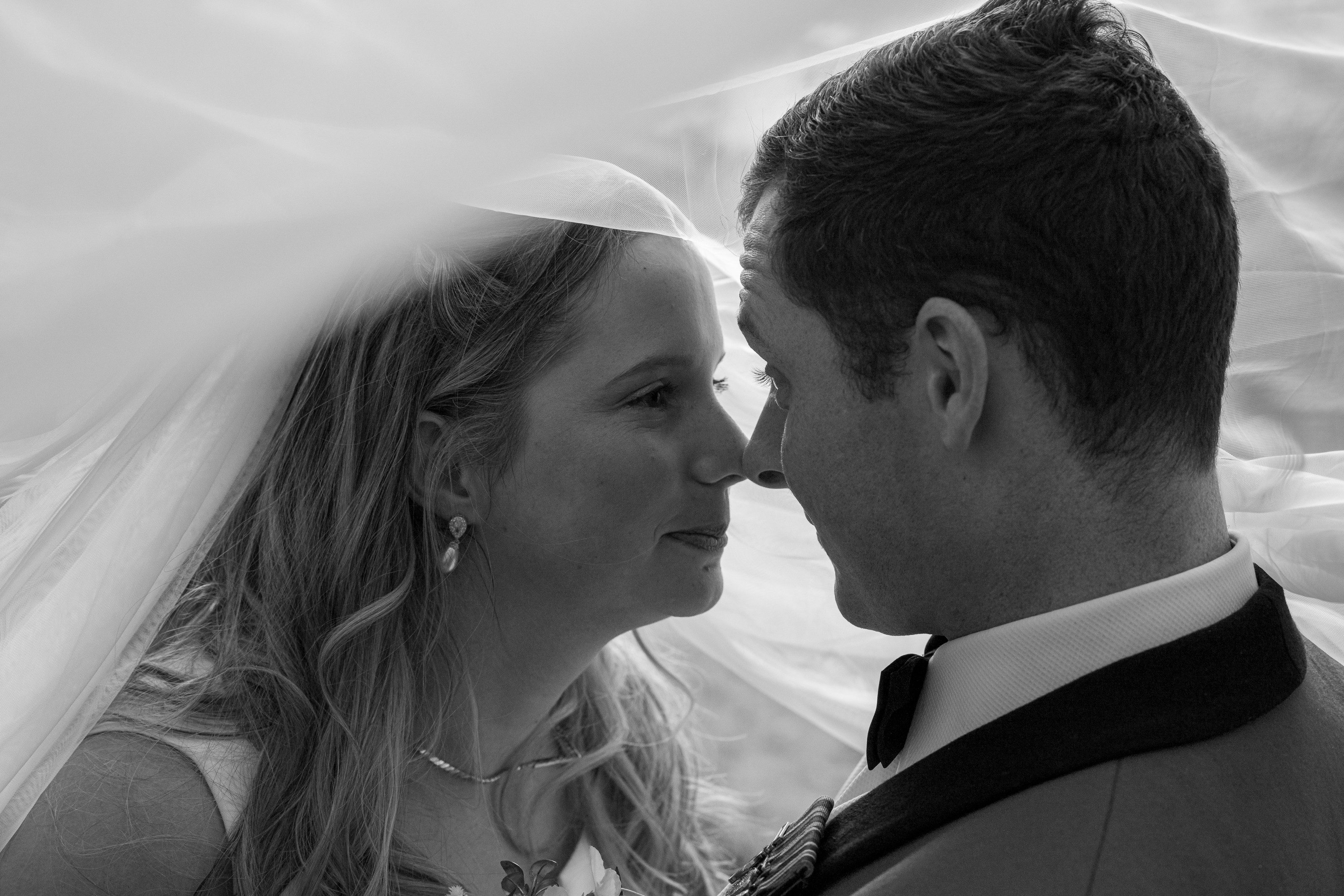 Bride and groom nose to nose beneath her veil, photographed in black and white