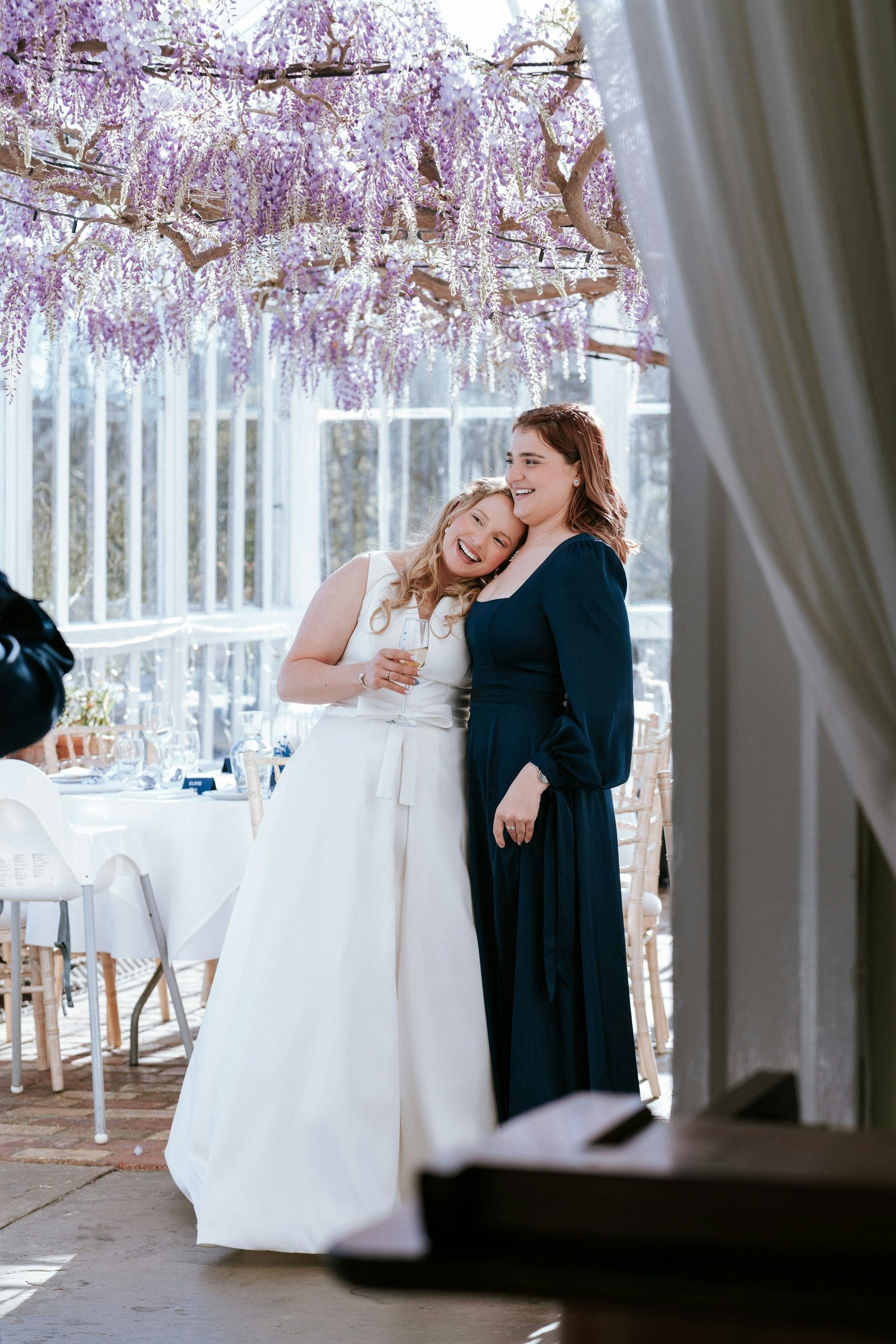 Bride and her mother beneath wisteria at the reception