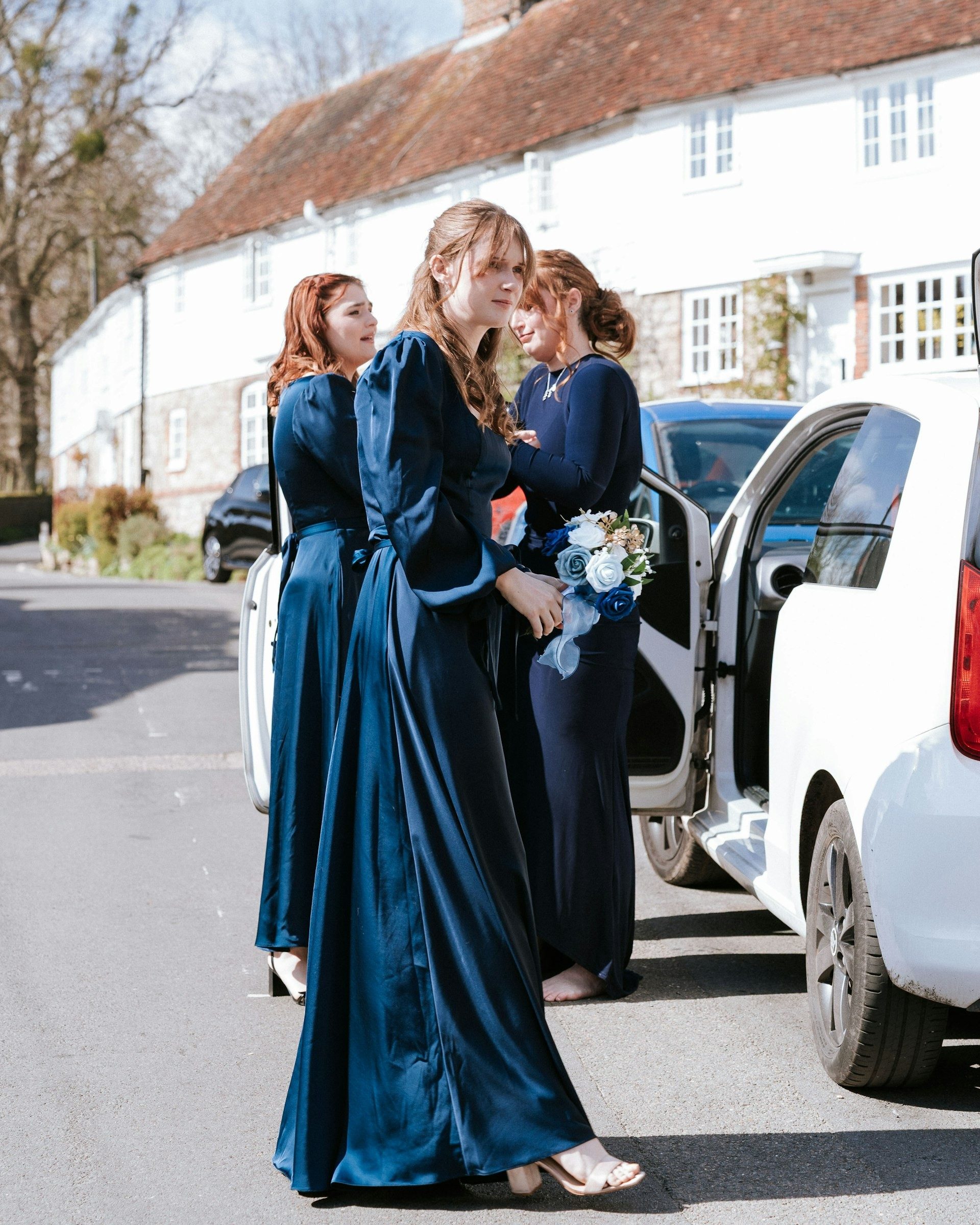 Bridesmaids in navy step out of the car outside the church
