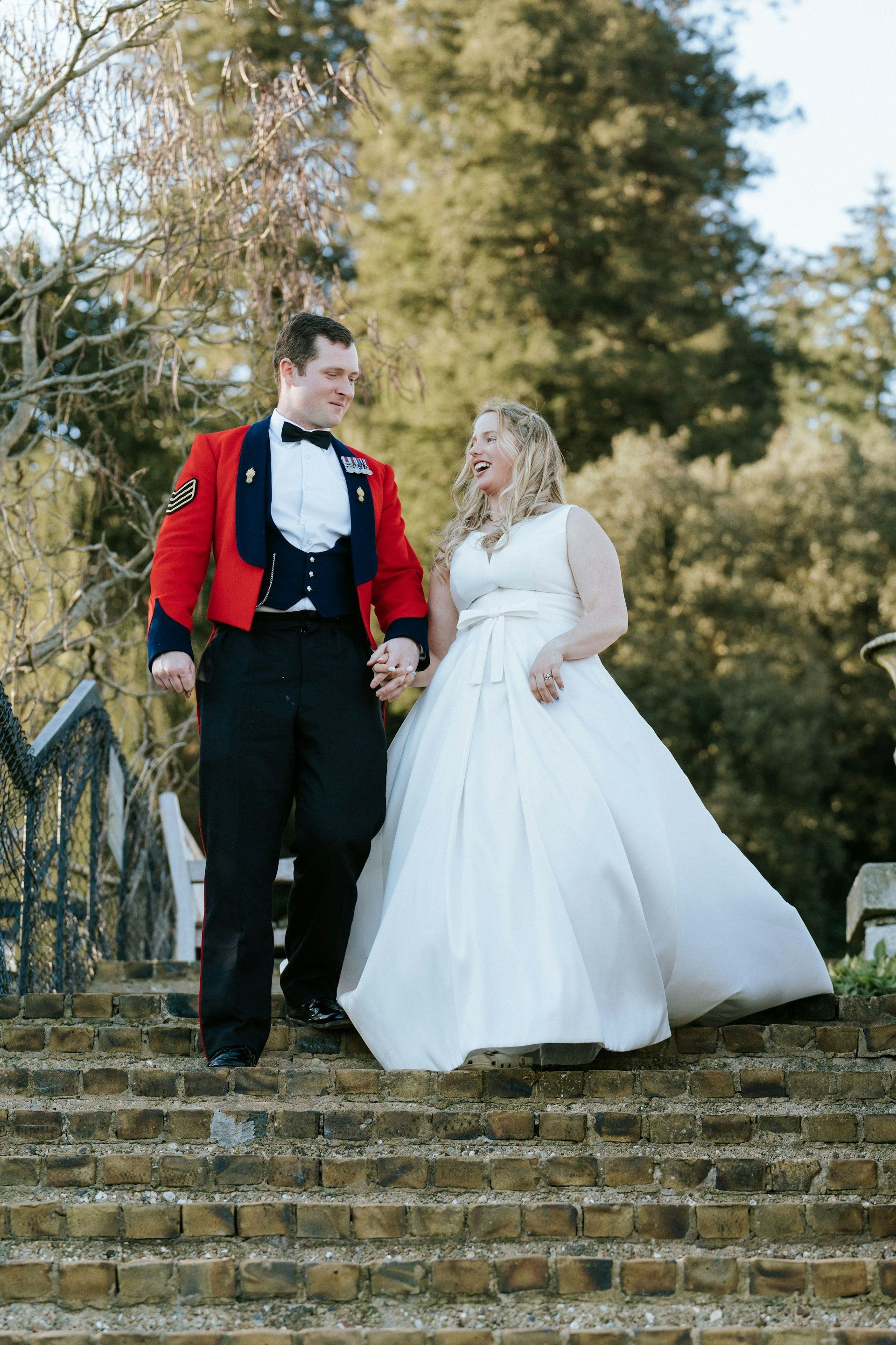 Bride and groom walk hand in hand down brick garden steps