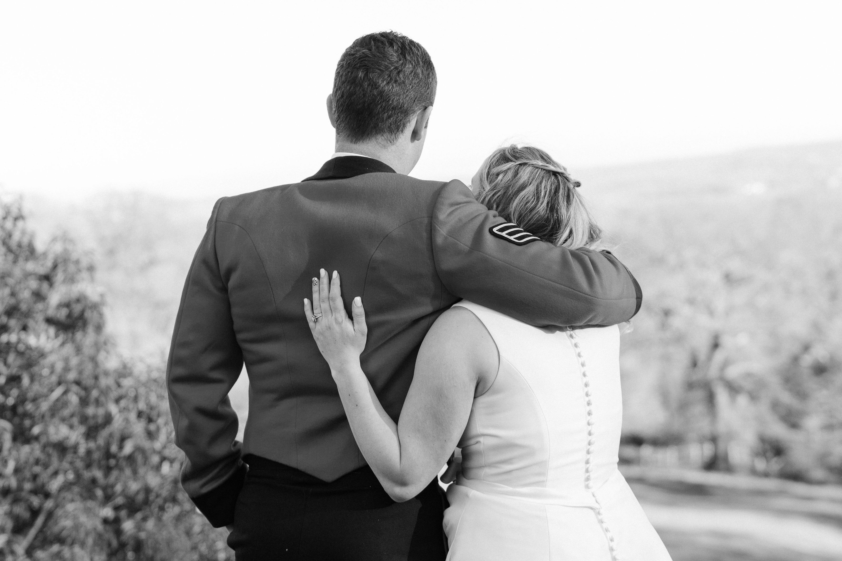 Groom wraps his bride in an embrace looking out across the hills, in black and white