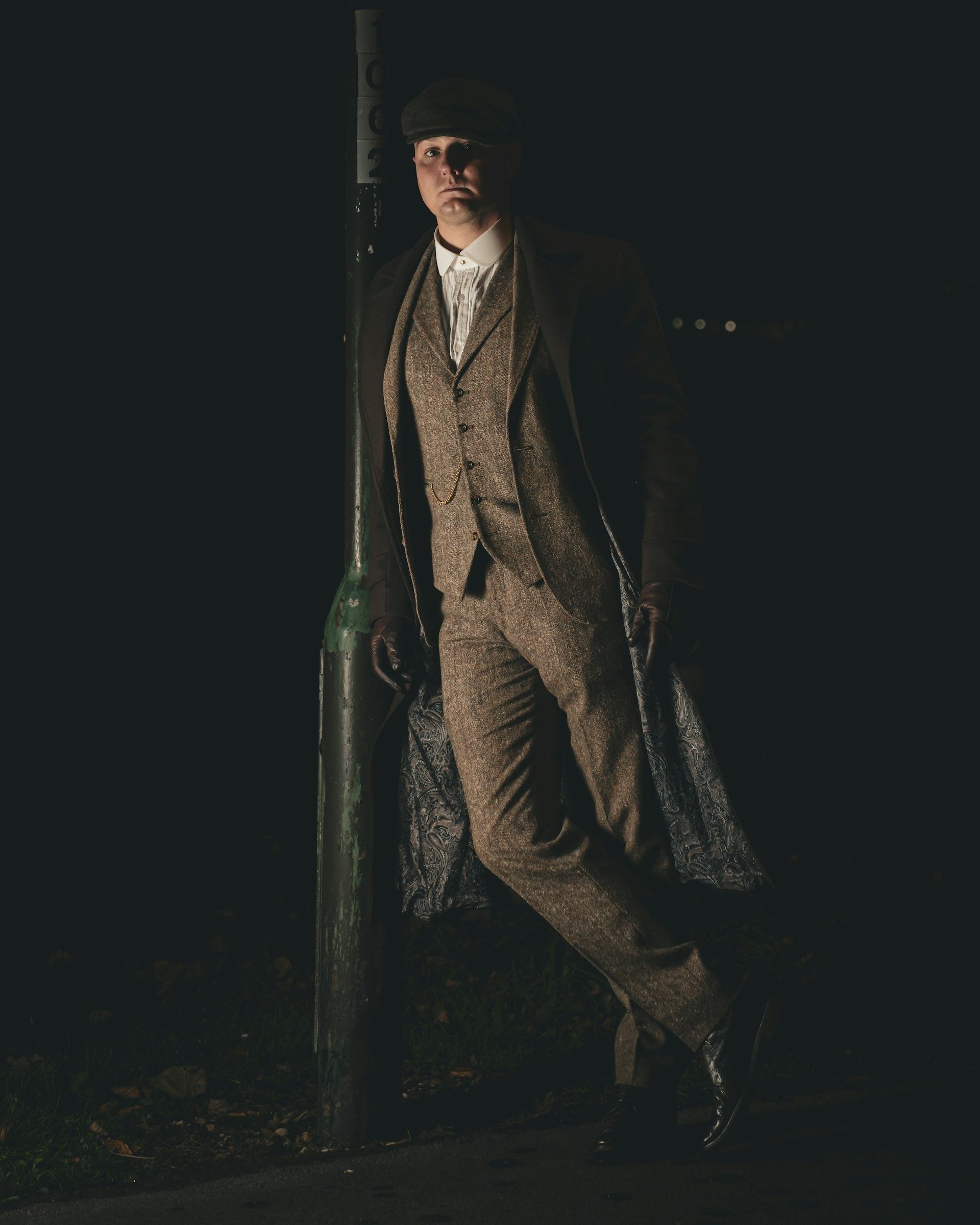 Man in tweed leans against a lamp post at night