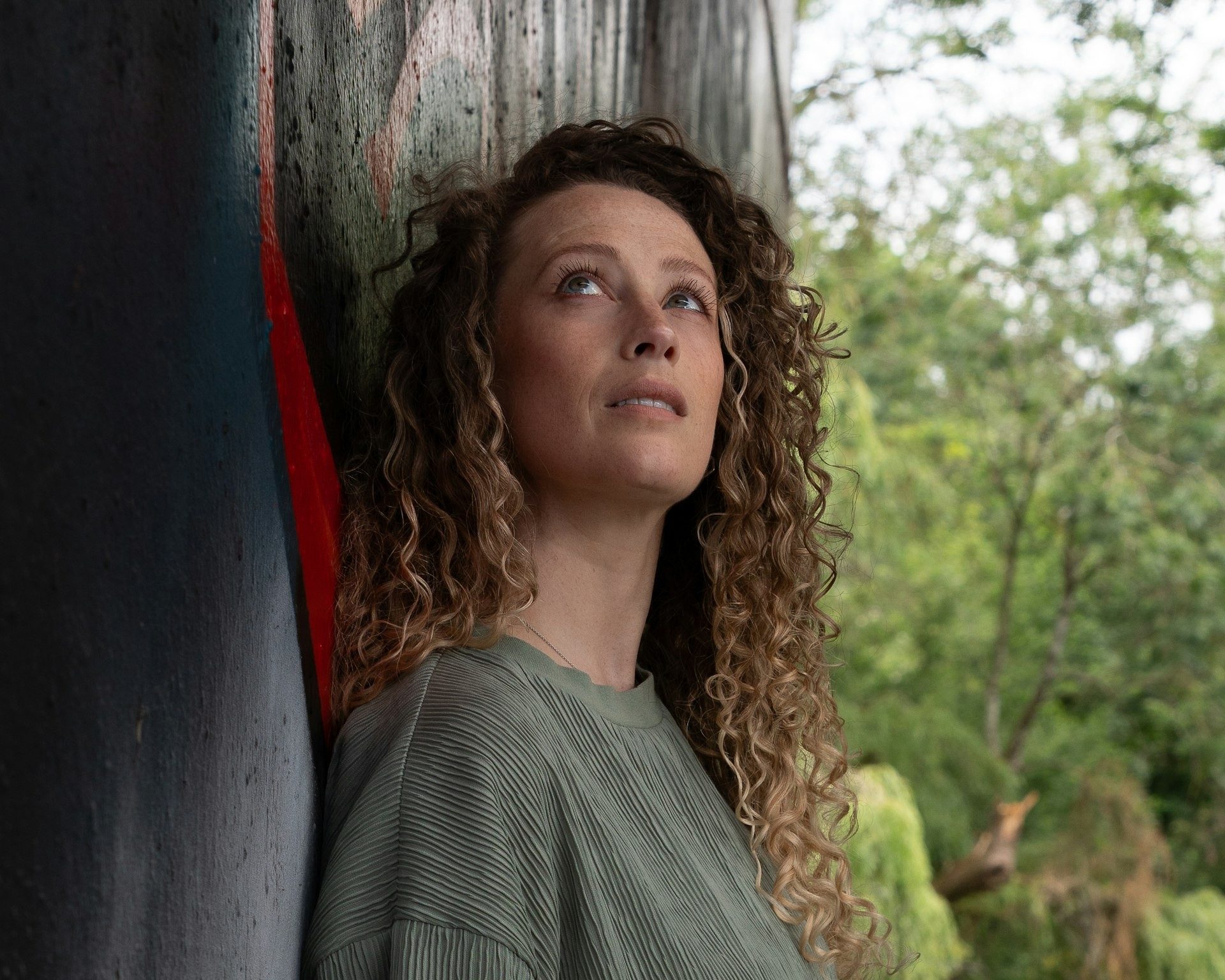 Woman in green leans against a wall and looks up