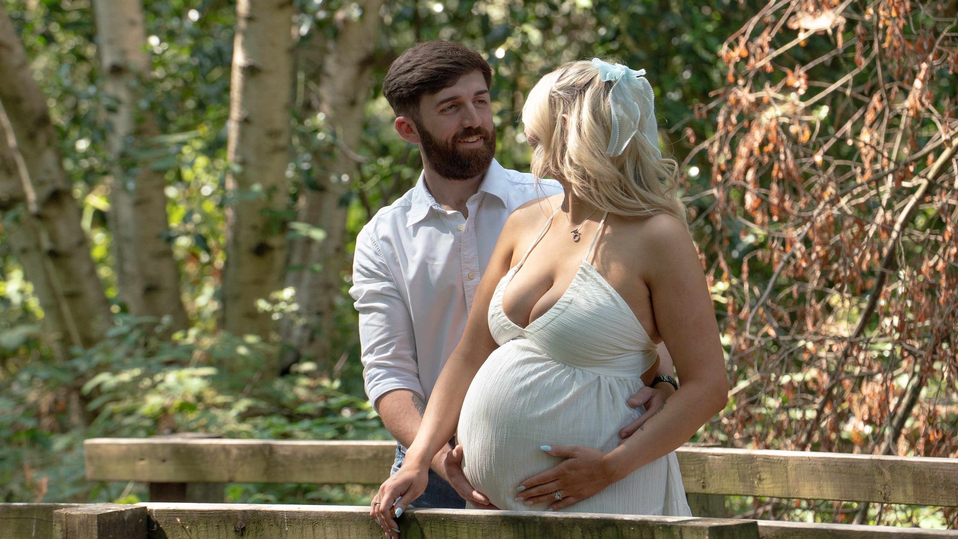 Expectant couple share a look on a woodland footbridge