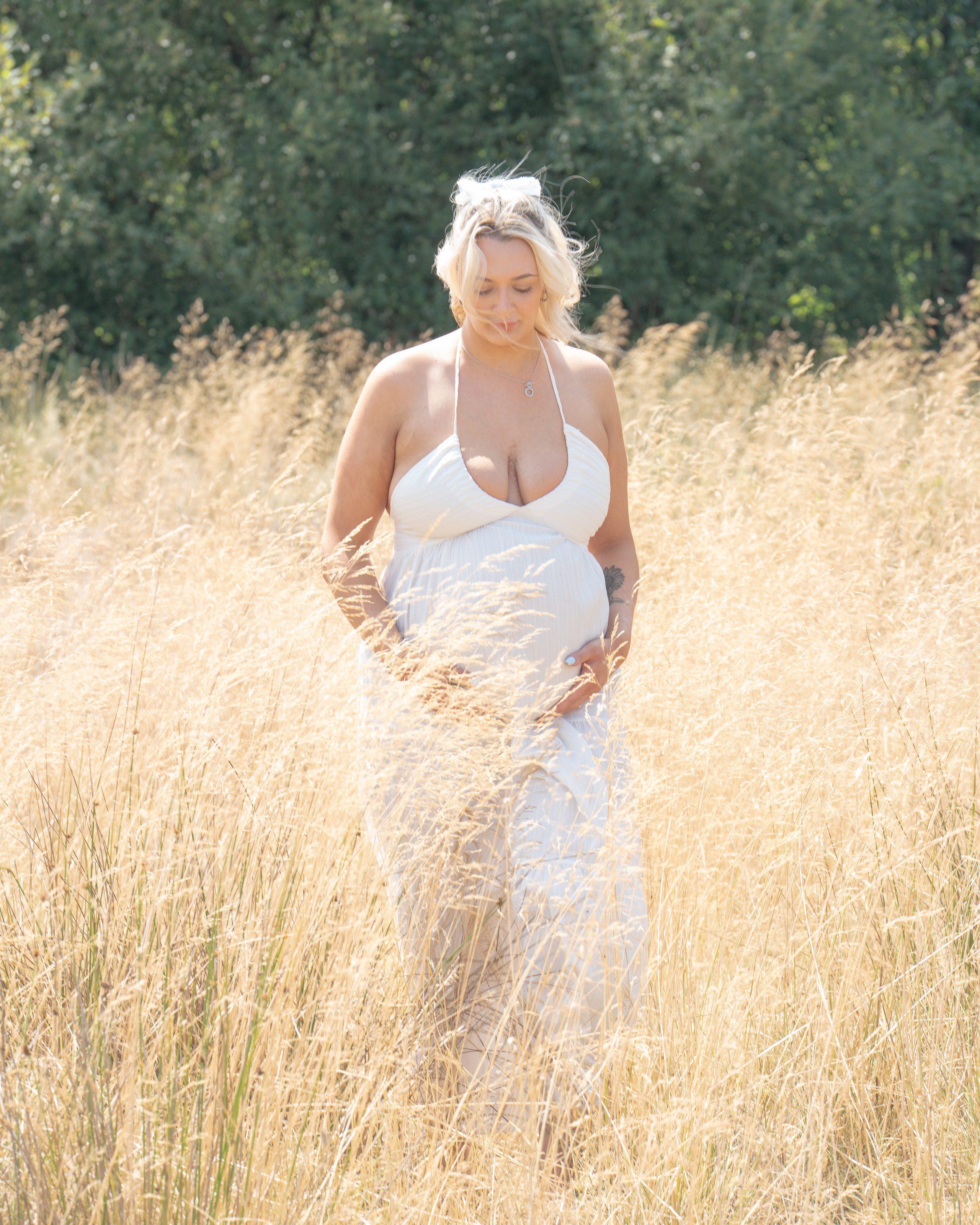 Expectant mother cradles her bump among golden grasses