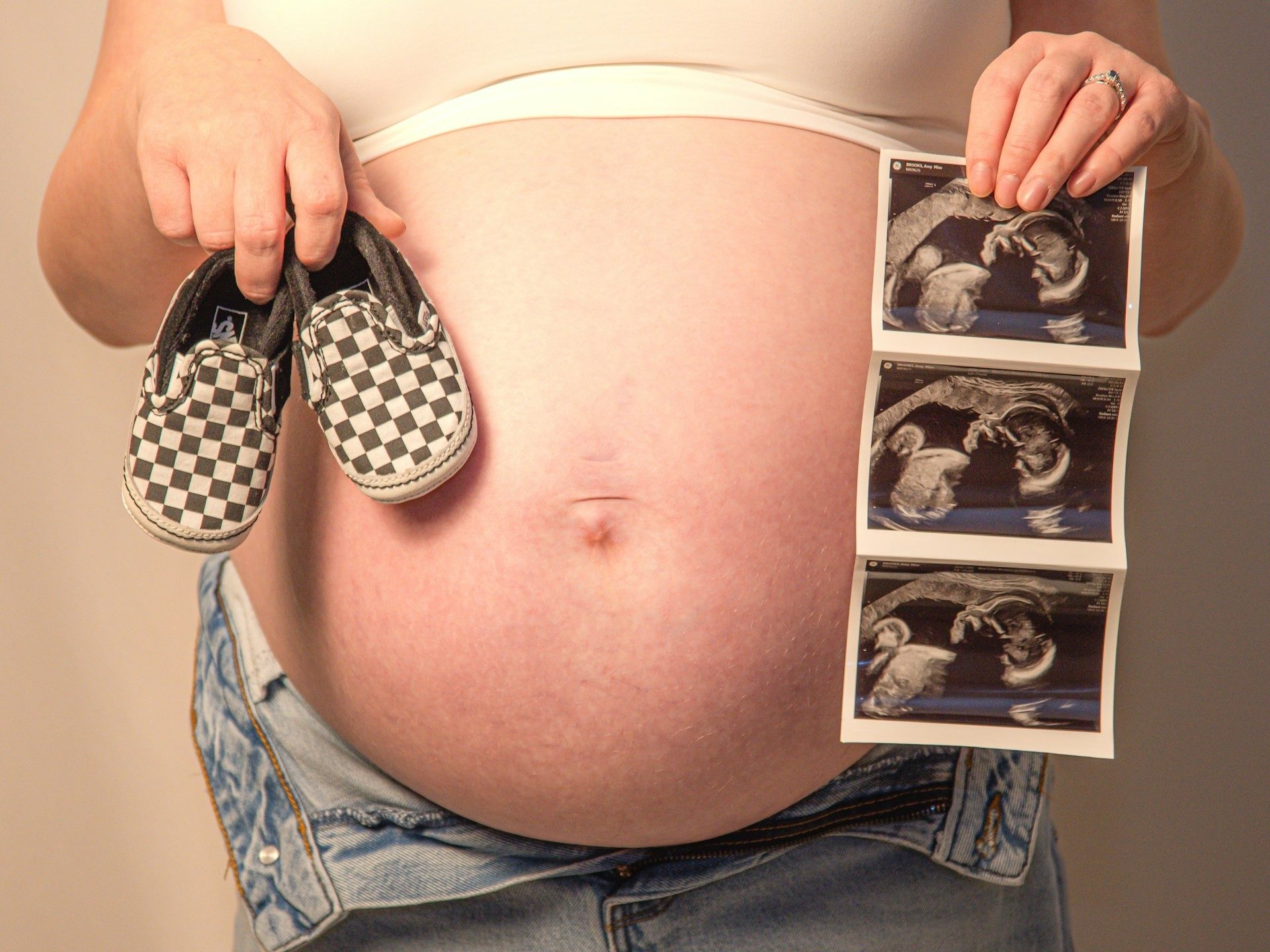 Expectant mother holds baby shoes and scan photos above her bump