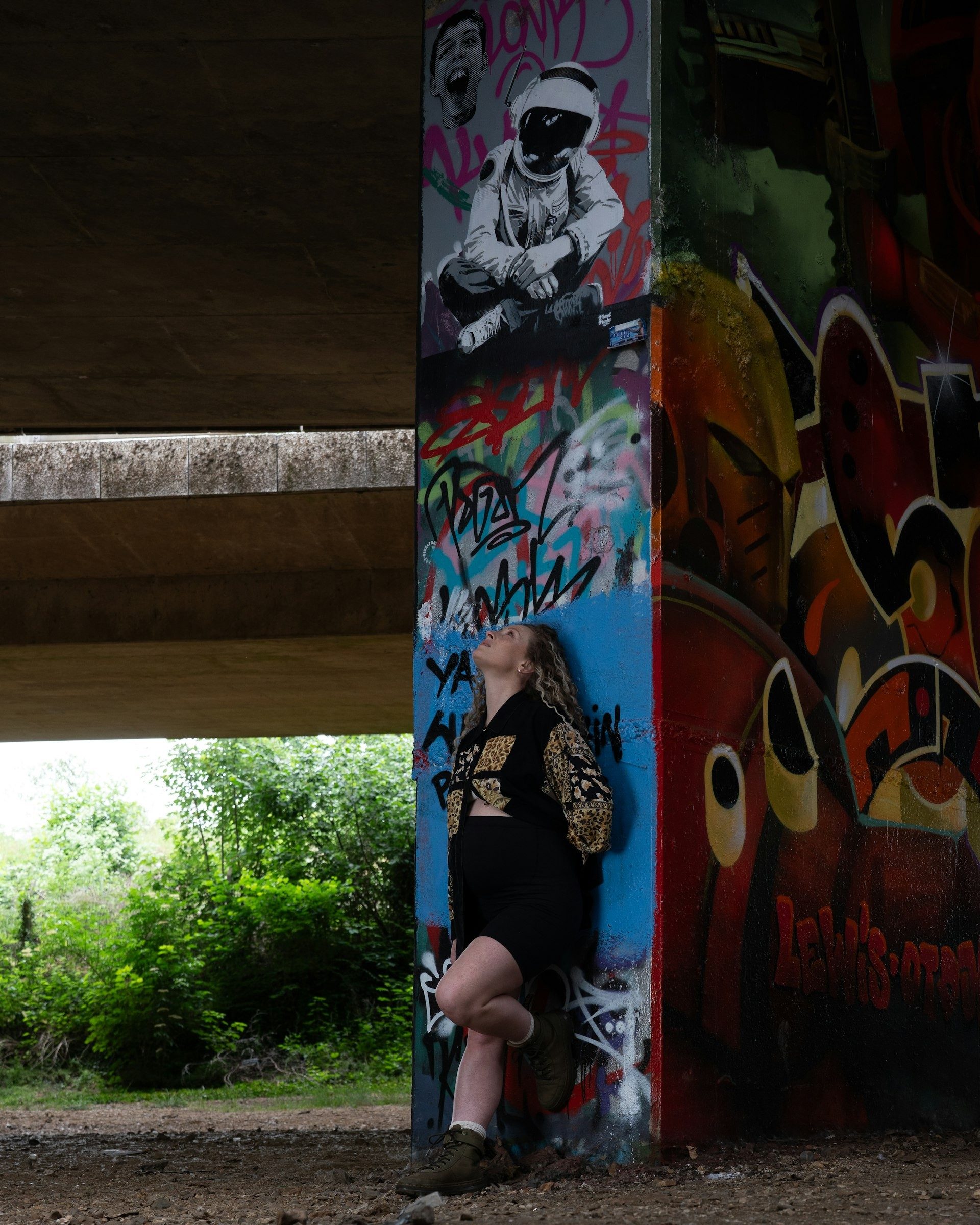 Expectant mother beside a graffiti wall under a bridge