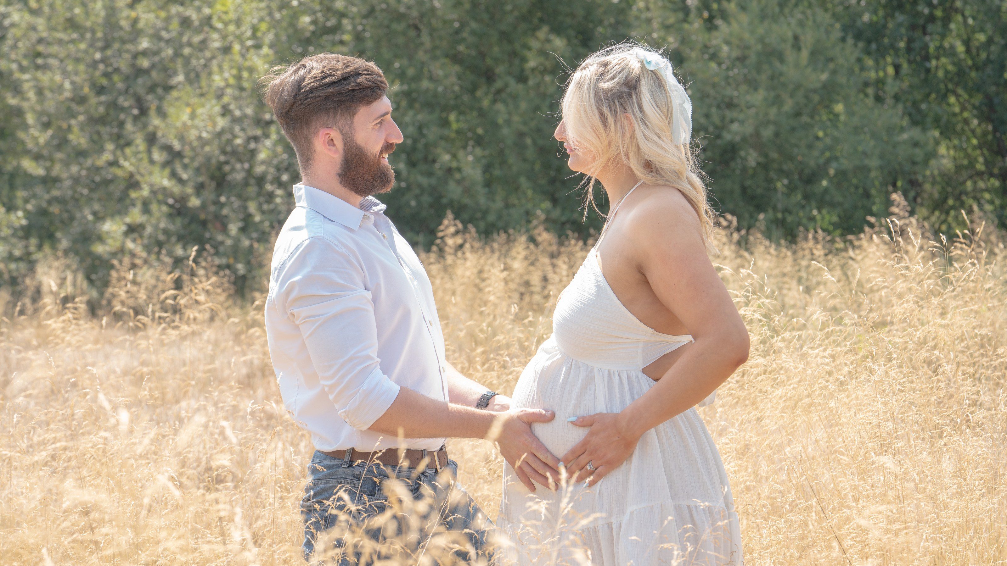 Expectant couple face each other in a summer meadow