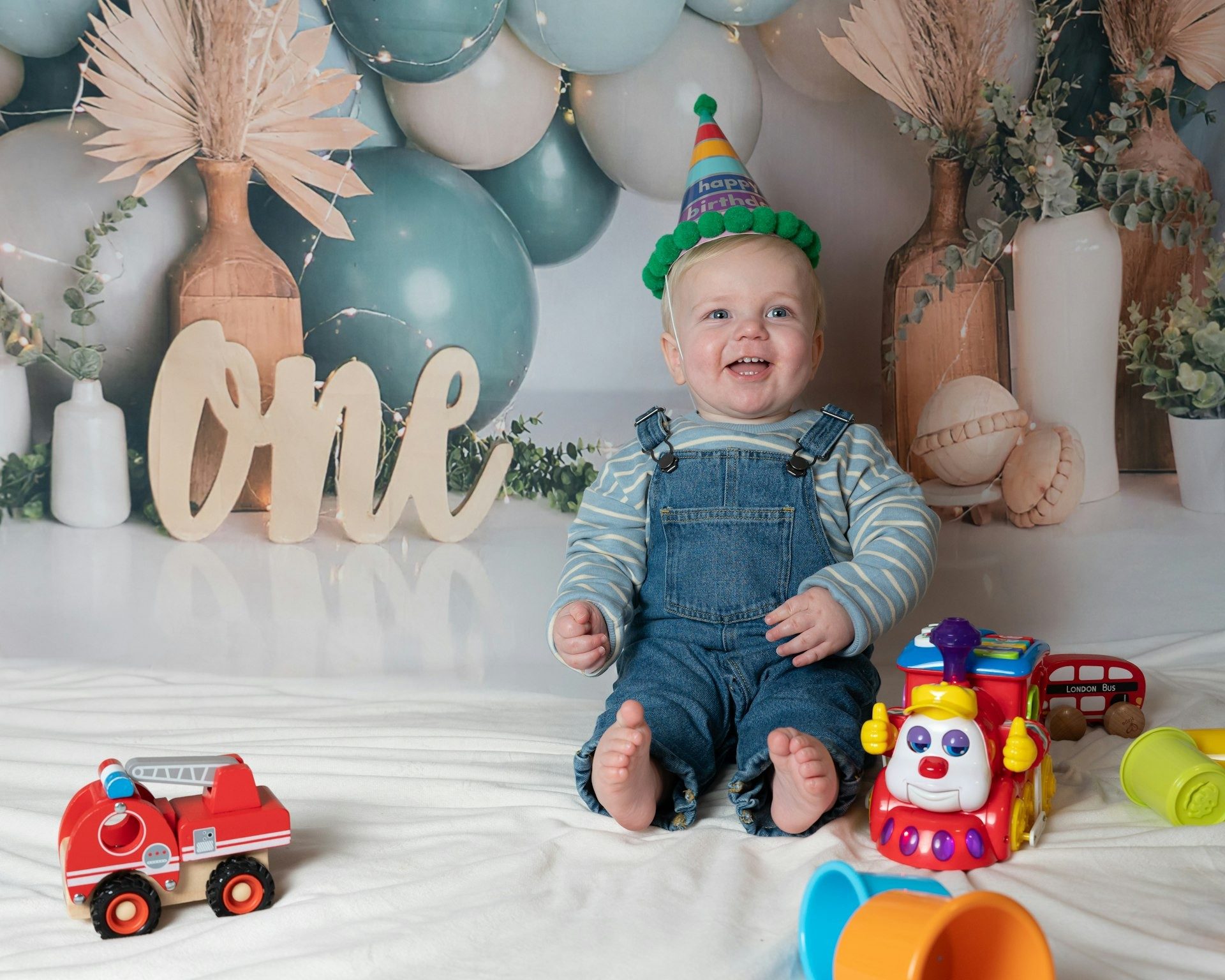 One year old sits among his toys beside a wooden “one” sign