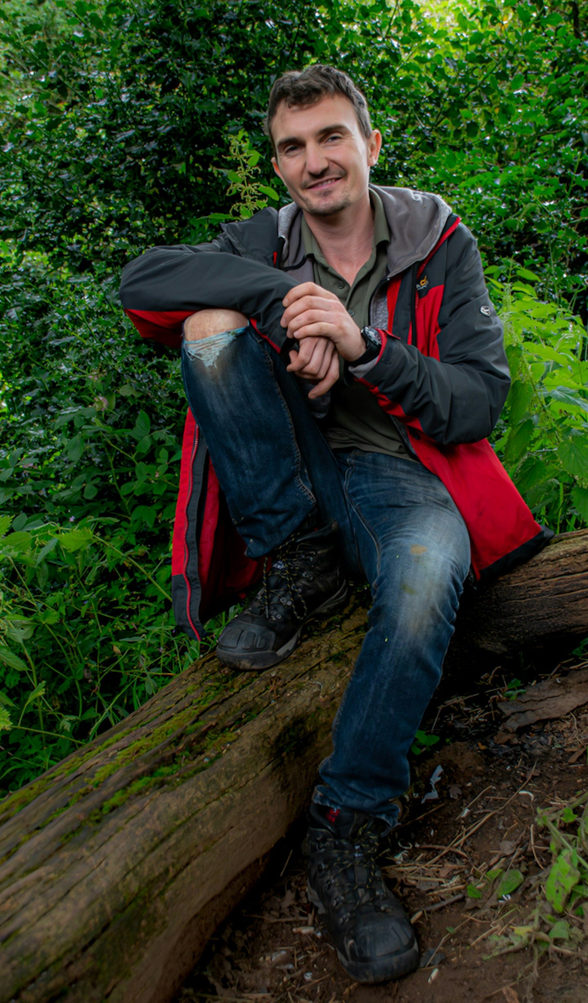 Man in outdoor gear crouches on a fallen log in the woods