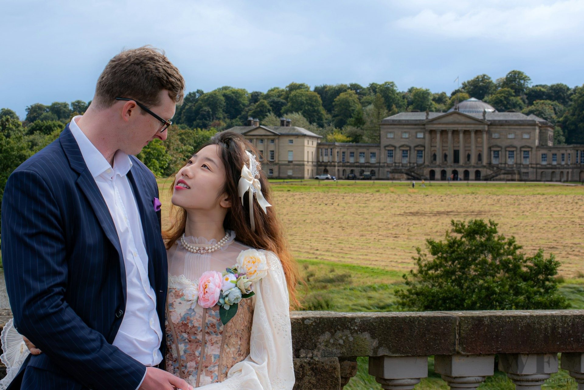 Bride and groom in parkland in front of a country house