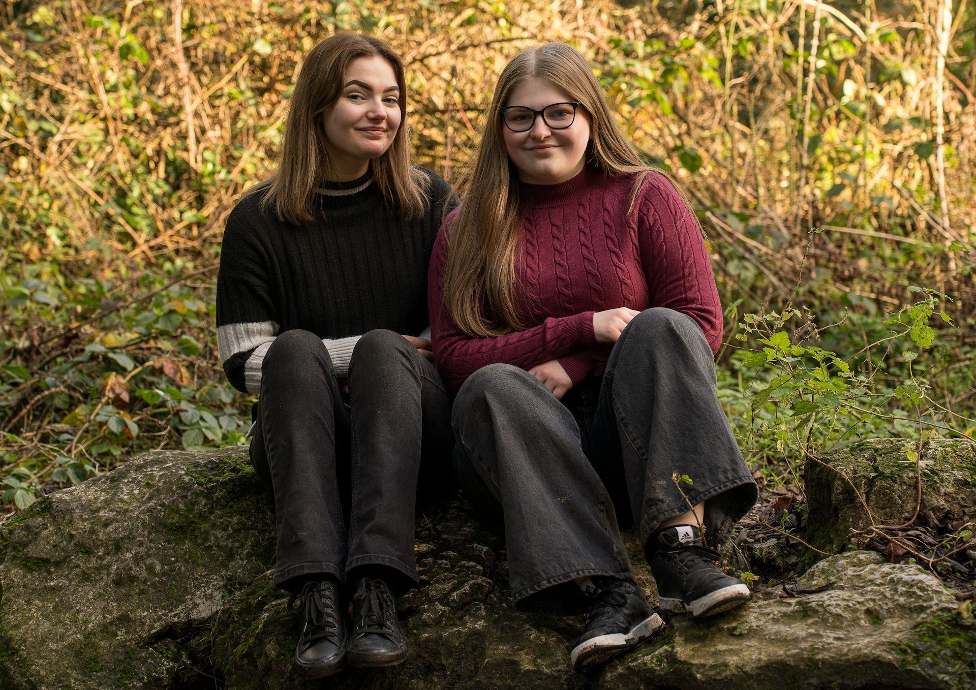 Two young women sit together on a woodland log