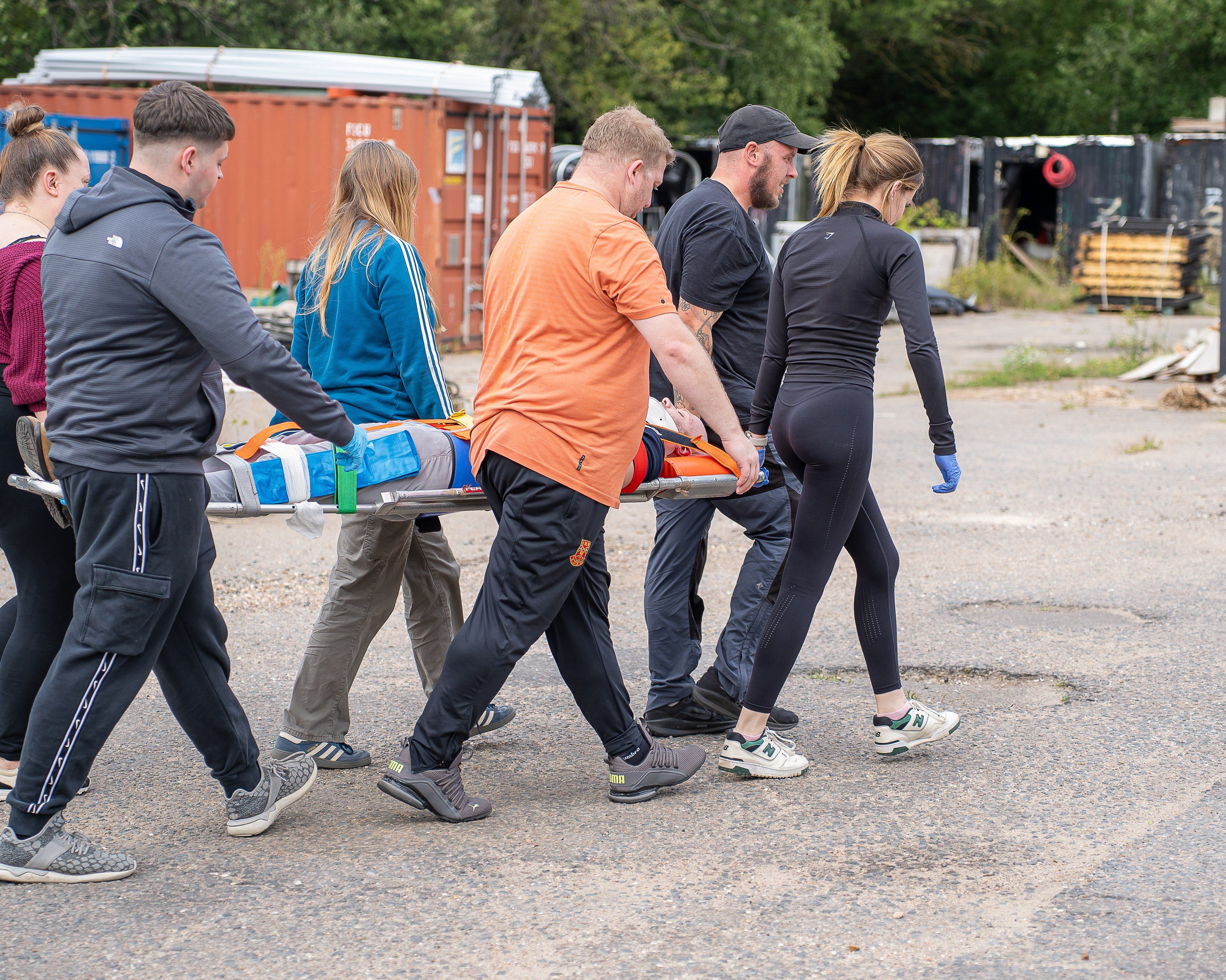 Trainees carry a casualty on a stretcher across the yard