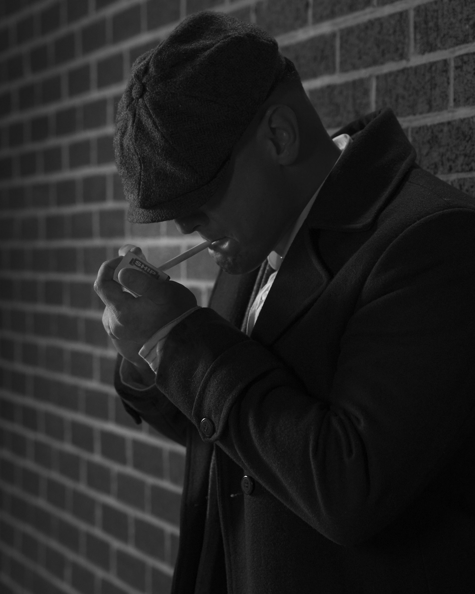 Man in a flat cap strikes a match, in black and white
