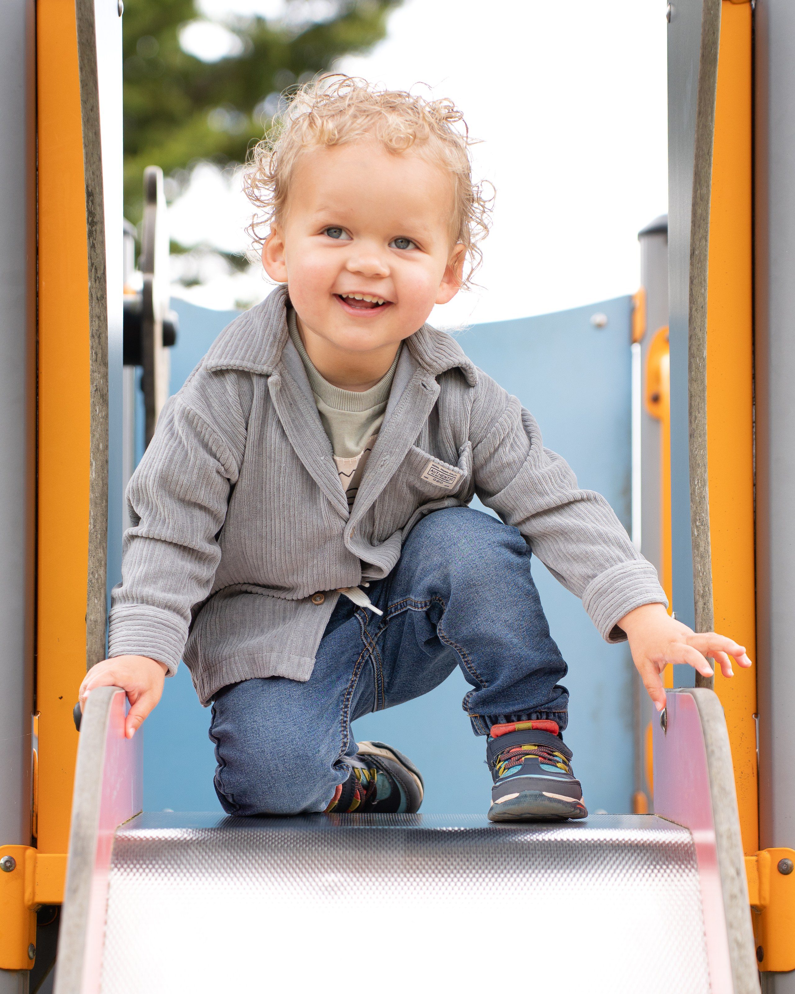 Toddler grins from the top of the playground slide
