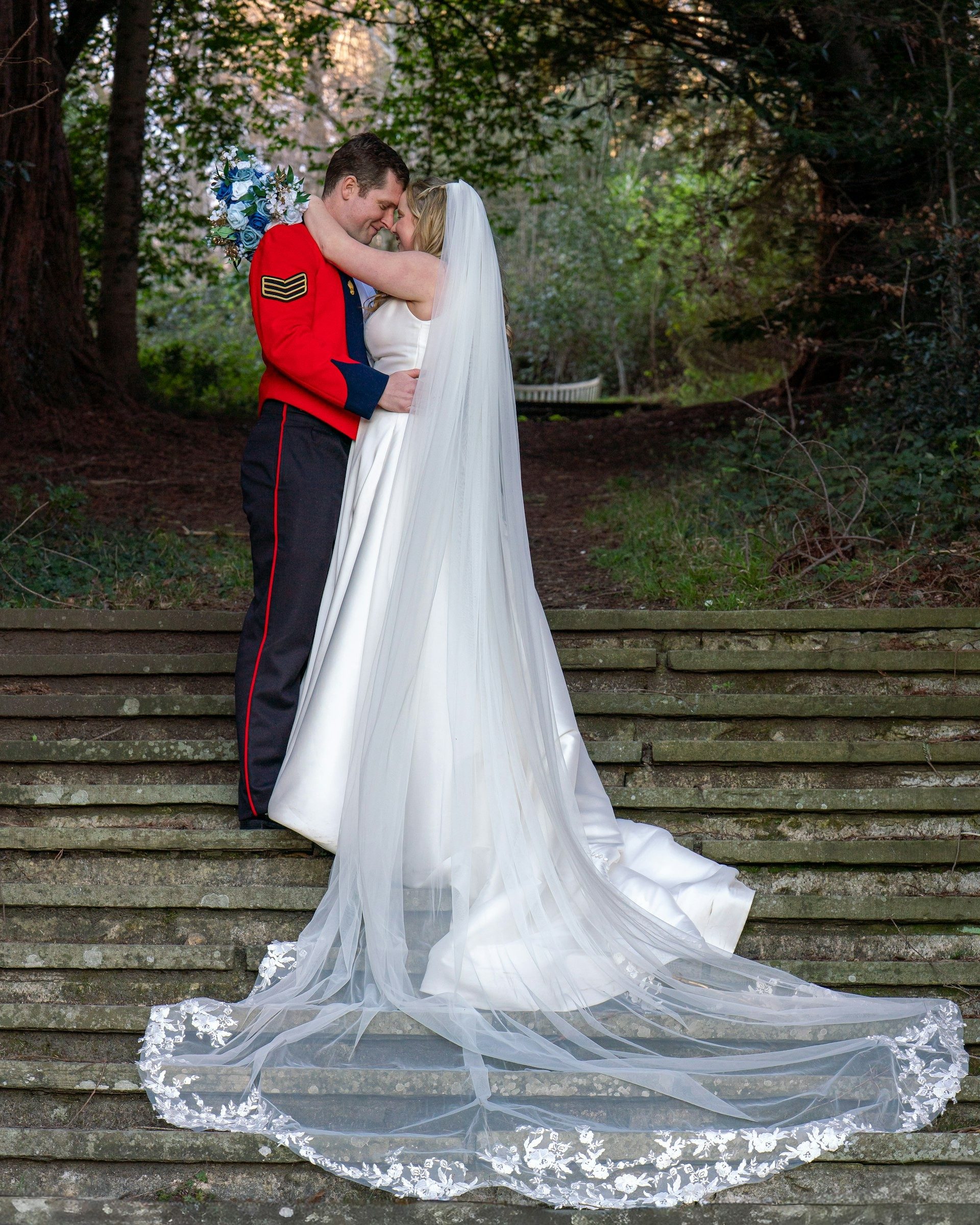 Bride and groom on woodland steps with her veil spread across them