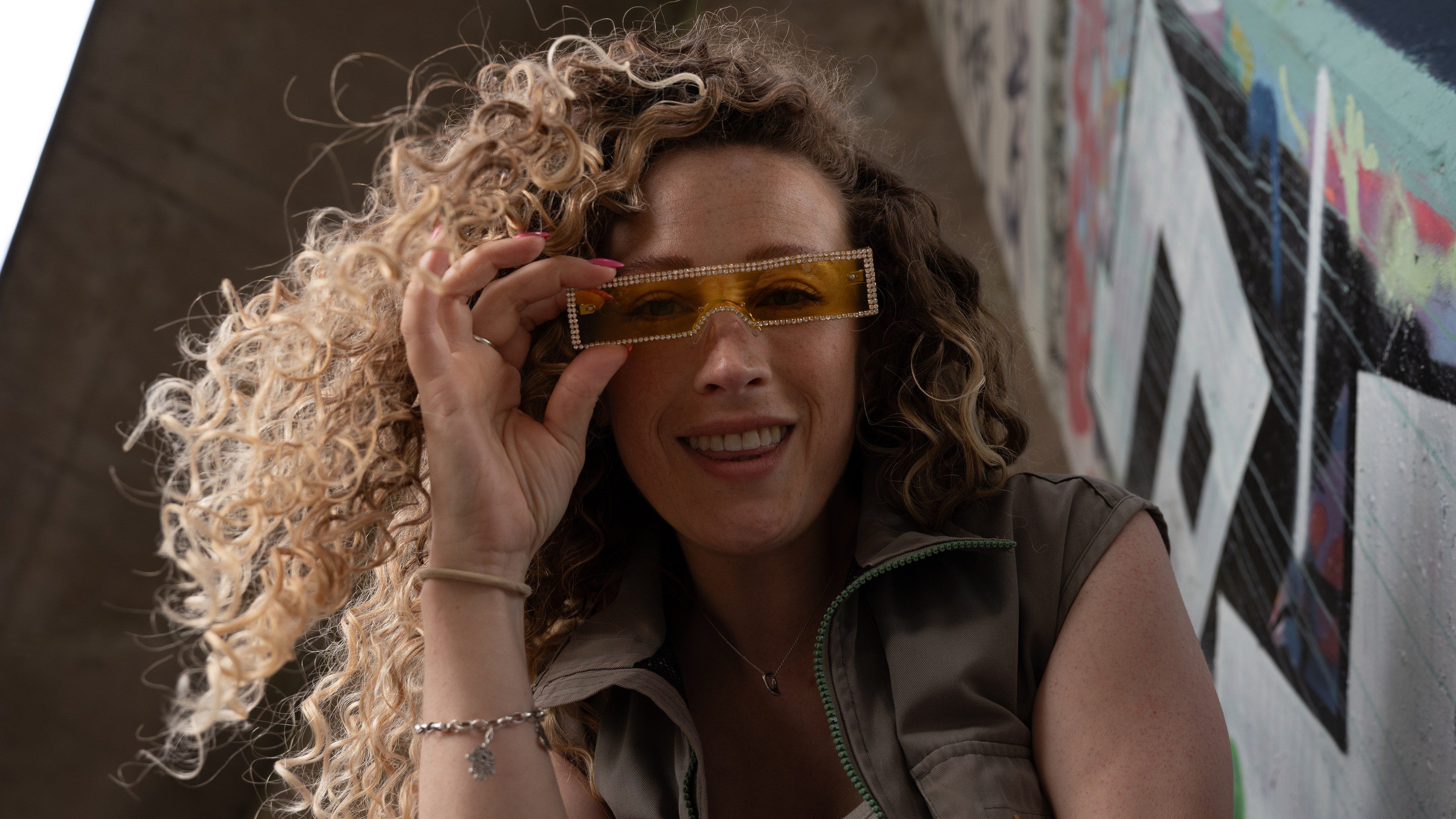 Model smiles over yellow sunglasses beneath the underpass